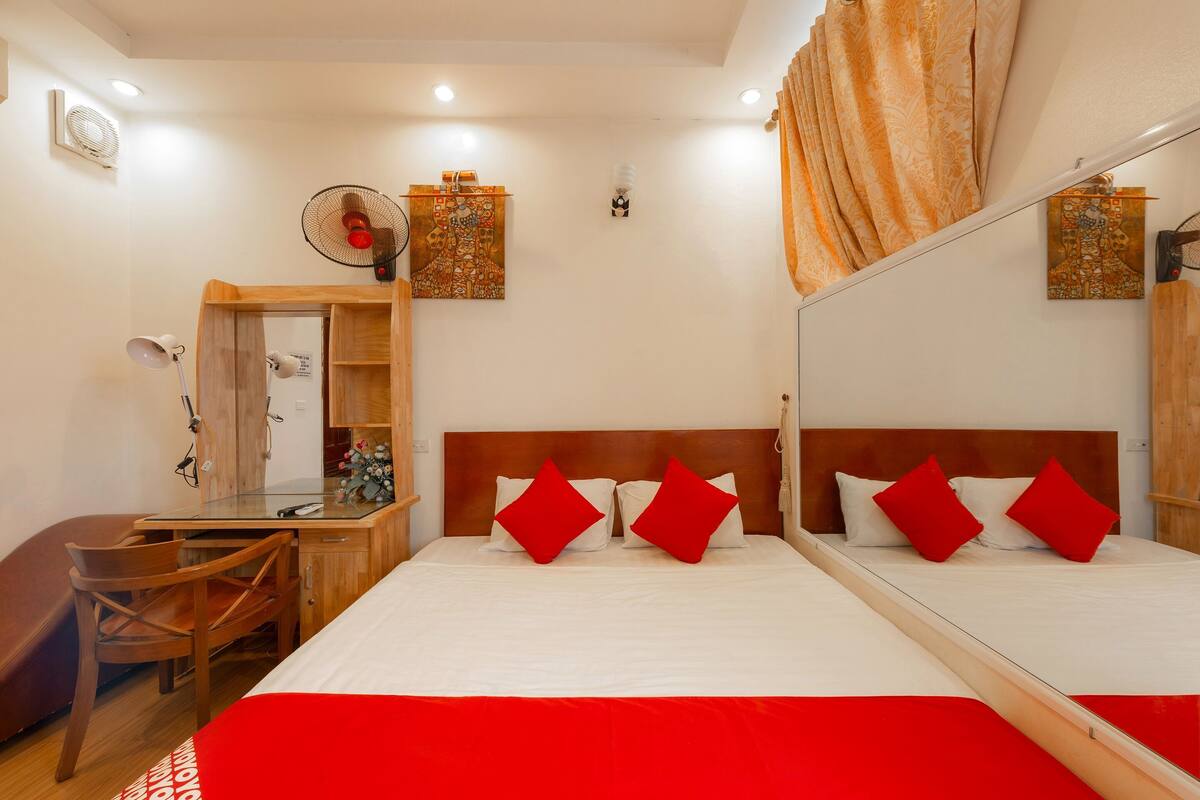 A hotel room with a bed, a desk, a chair, a mirror, and a wall-mounted fan.