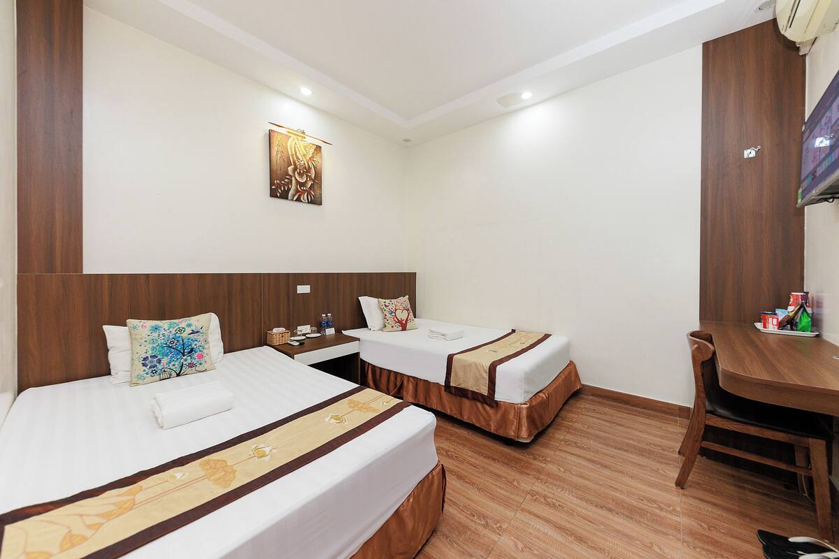 A hotel room with two beds, a wooden headboard, a desk, and a television.