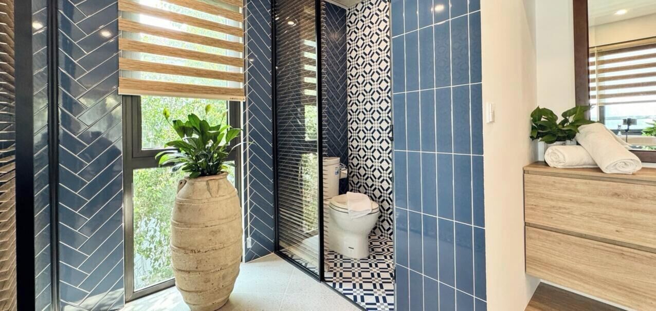 A modern bathroom with a large potted plant, a toilet, and a wooden vanity with towels.