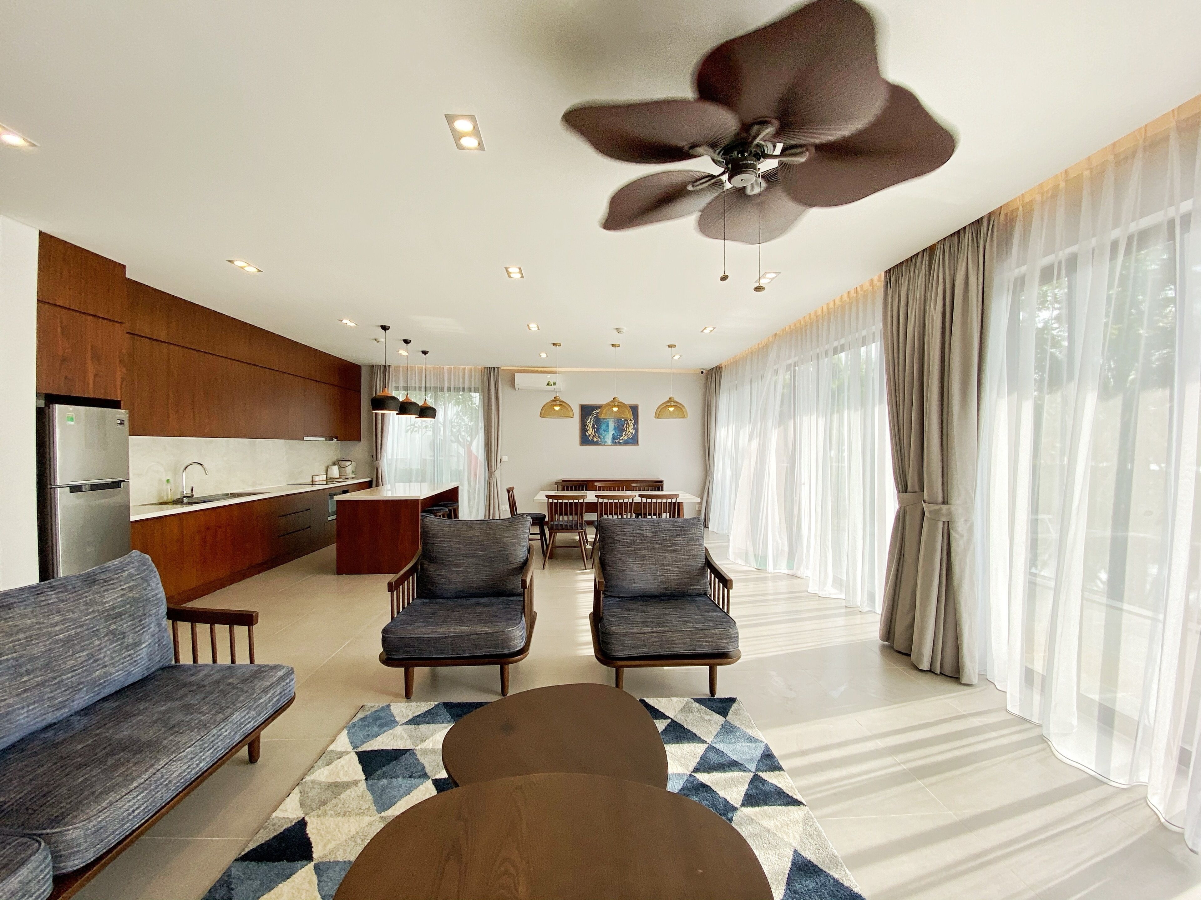 A modern living room with a sofa, two armchairs, a coffee table, and a dining area with a table and chairs.