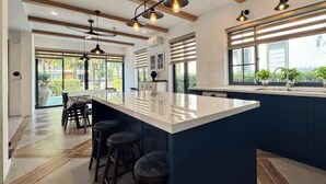 A modern kitchen with a large island, bar stools, and a view of the outdoors through large windows. - M Villas Phu Quoc (Phu Quoc)