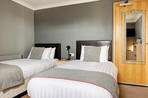 A hotel room with two beds, a wooden wardrobe, and a mirror.