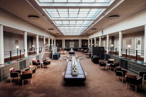 A spacious hotel lobby with a high ceiling, skylights, and a central seating area.