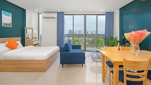 A modern hotel room with a bed, a sofa, a dining table, and a balcony with a city view.