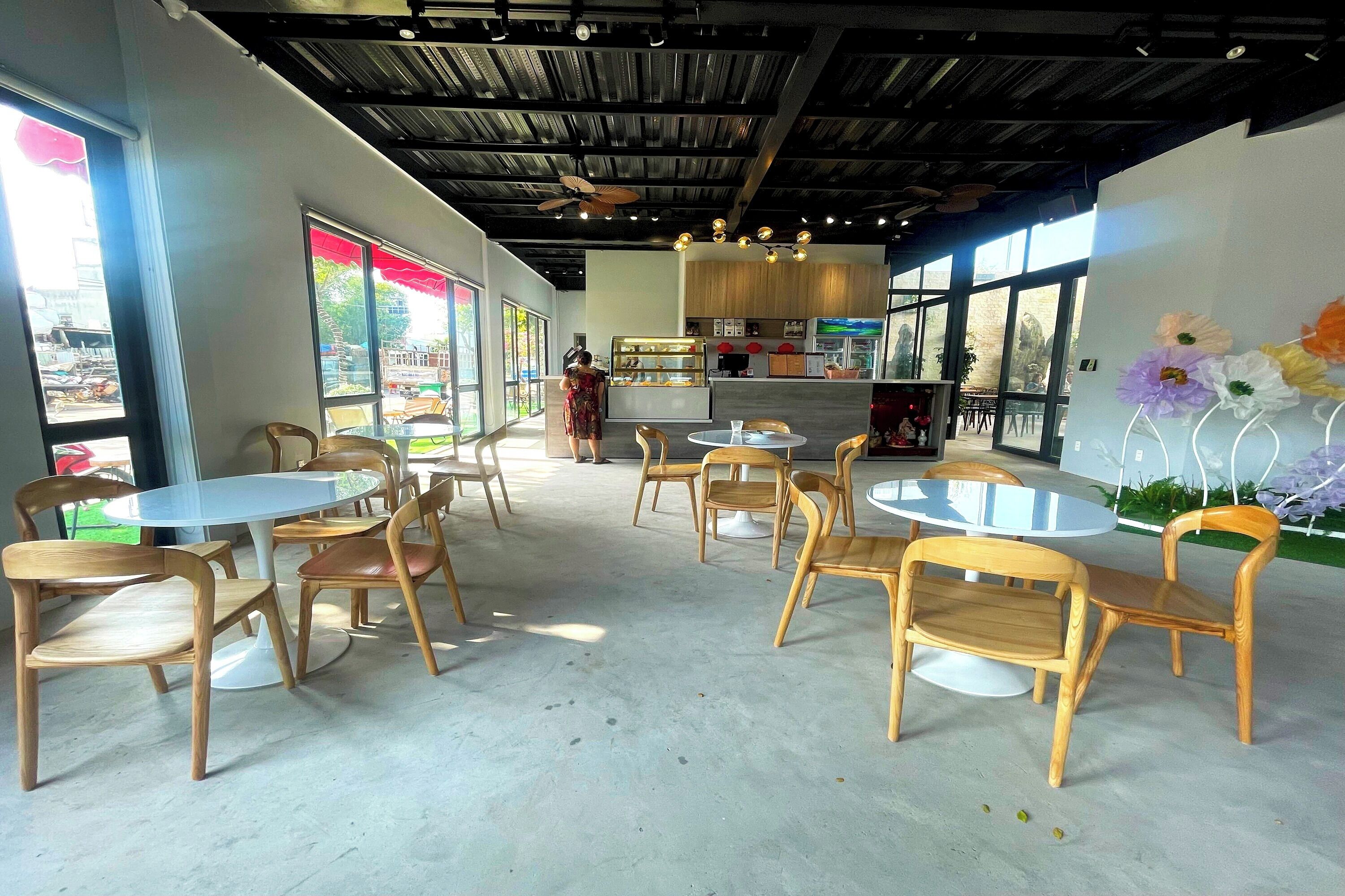 A cafe with round tables and wooden chairs, large windows with a view, and a ceiling with exposed beams.