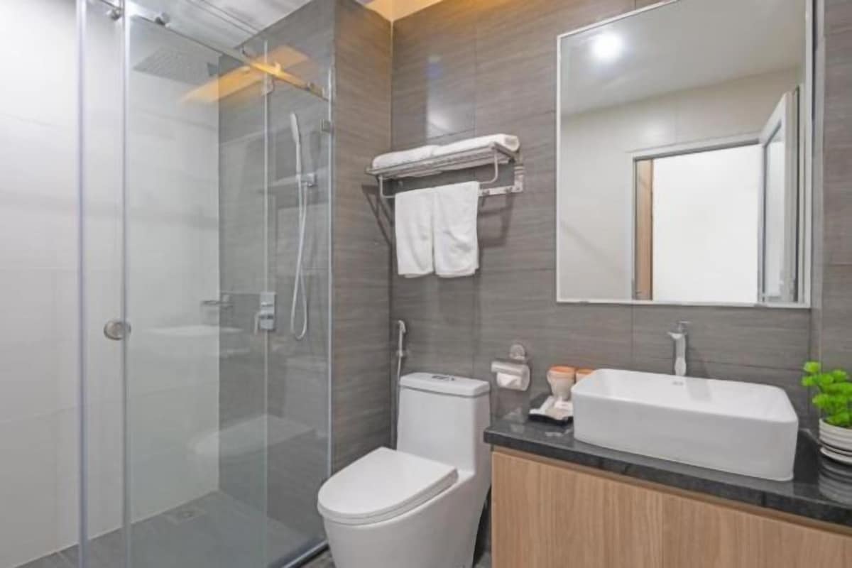 A modern bathroom with a glass shower enclosure, a white toilet, a sink with a mirror above it, and a towel rack with two towels.
