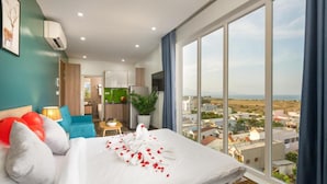 A hotel room with a large bed, a view of the city, and a kitchenette.