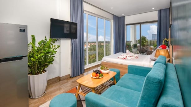 A modern hotel room with a bed, a TV, a balcony, and a dining area with a table and chairs.
