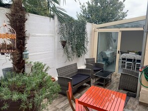 Eine Terrasse mit Korbmöbeln, eine Glastür zu einem Innenbereich und eine weiße Wand mit Kletterpflanzen.