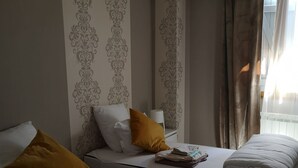 A hotel room with two beds, each with white bedding and a single brown pillow. The room has patterned wallpaper and a window with curtains. - GITE 7/8 P. LE NAPOLEON, Not suitable for PRMs (Saint-Leu-la-Forêt)
