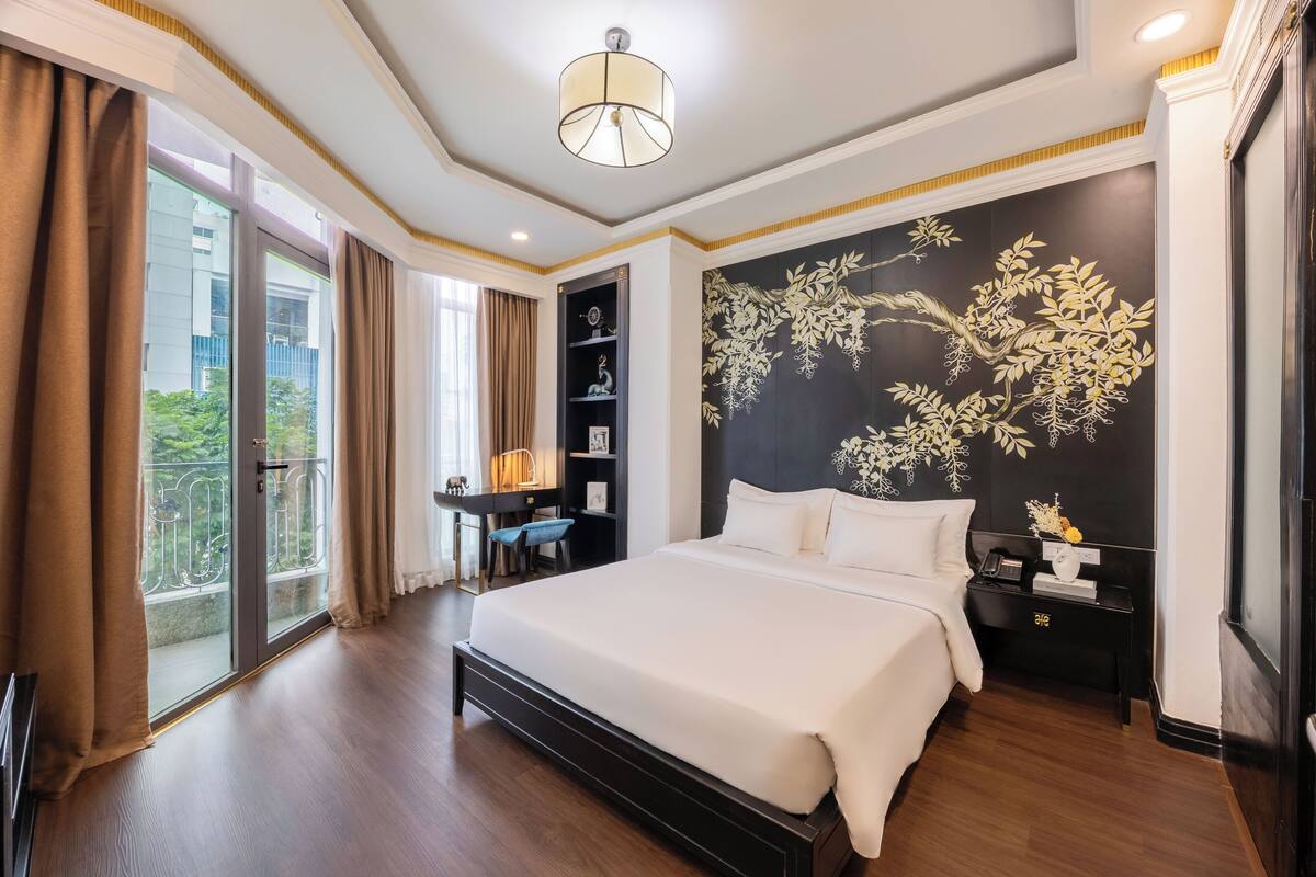 Ein Hotelzimmer mit einem großen Bett, einem Schreibtisch mit Stuhl, einem Bücherregal und einer Wanddekoration.