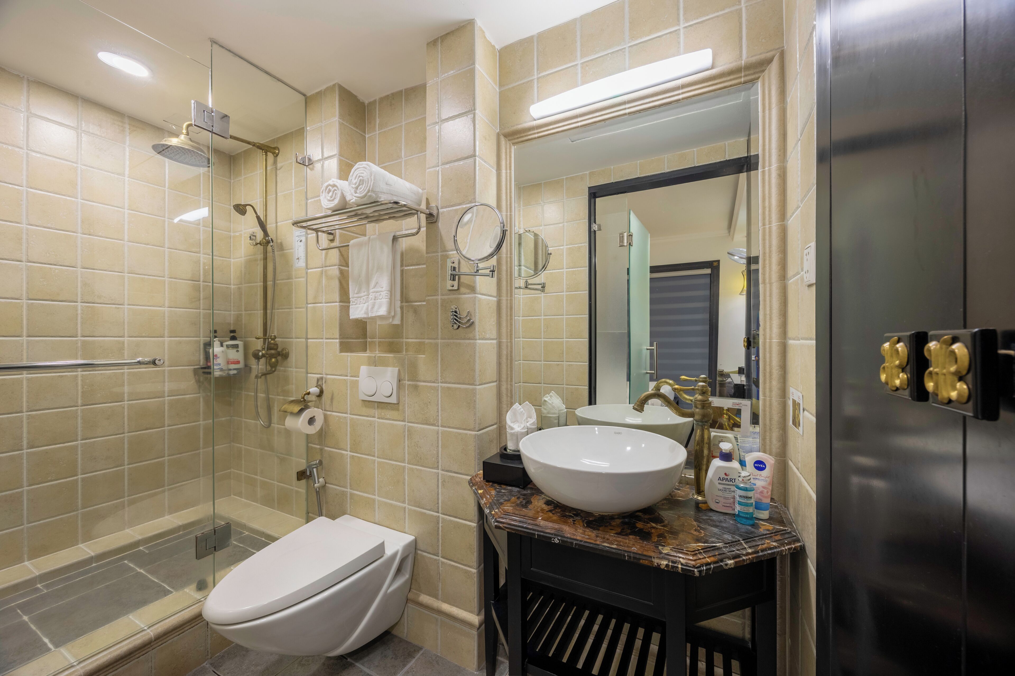 A modern bathroom with a glass shower enclosure, a white toilet, a sink with a marble countertop, and a large mirror.