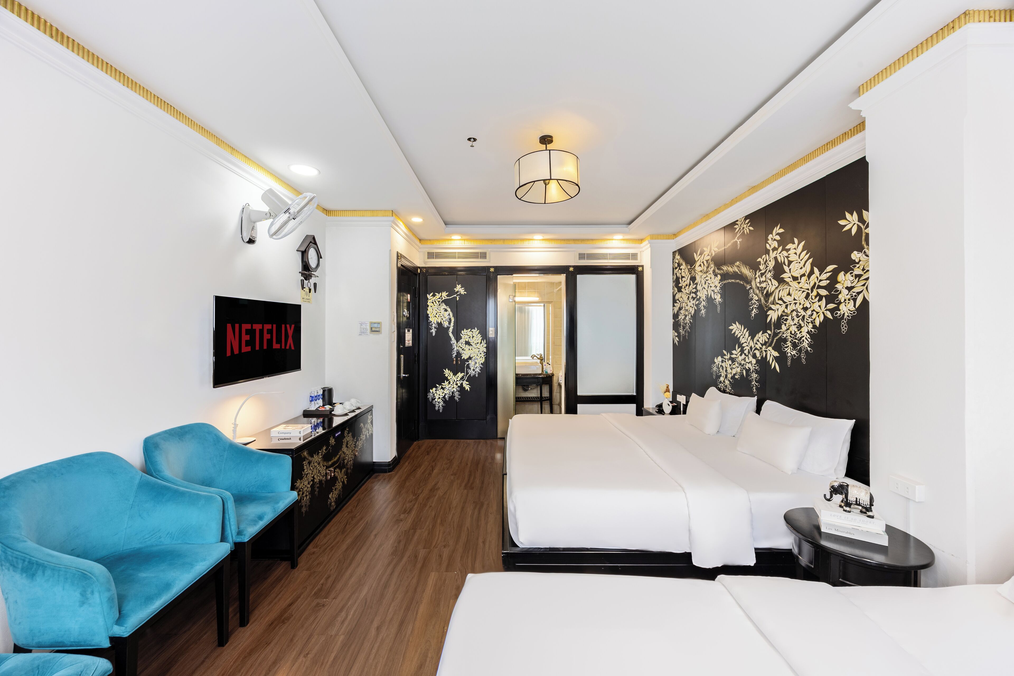 Habitación de hotel con cama, escritorio, silla, televisor y pared con diseño floral.