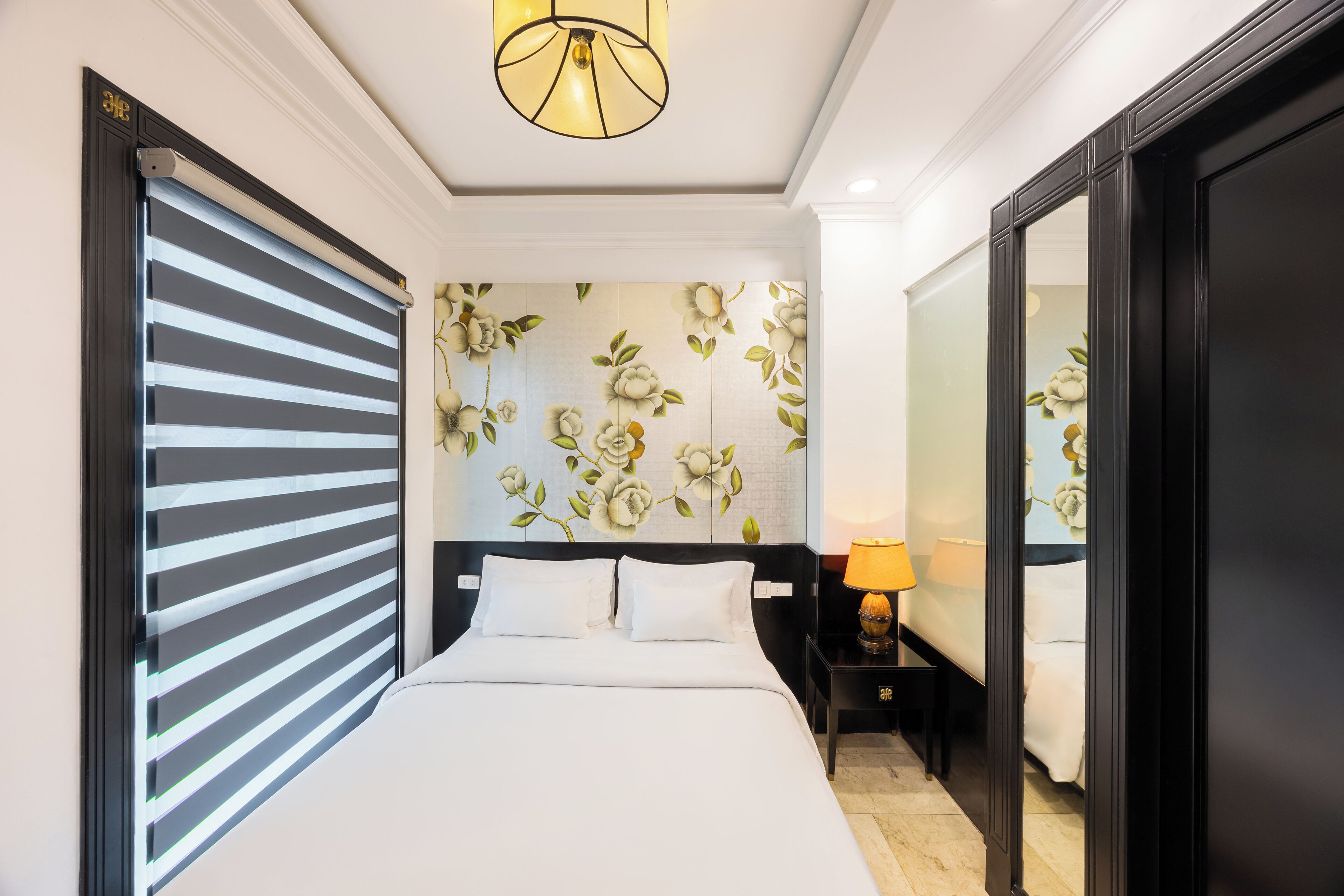 Une chambre d’hôtel avec un lit, une table de chevet avec une lampe, un miroir et un papier peint à motifs floraux.
