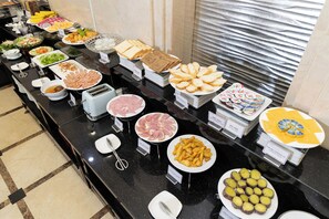 Een buffet met diverse gerechten, waaronder vleeswaren, kazen en fruit.