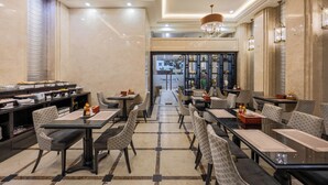 Une salle à manger d’hôtel avec plusieurs tables et chaises, un buffet situé à gauche et une vue sur la rue depuis l’entrée.