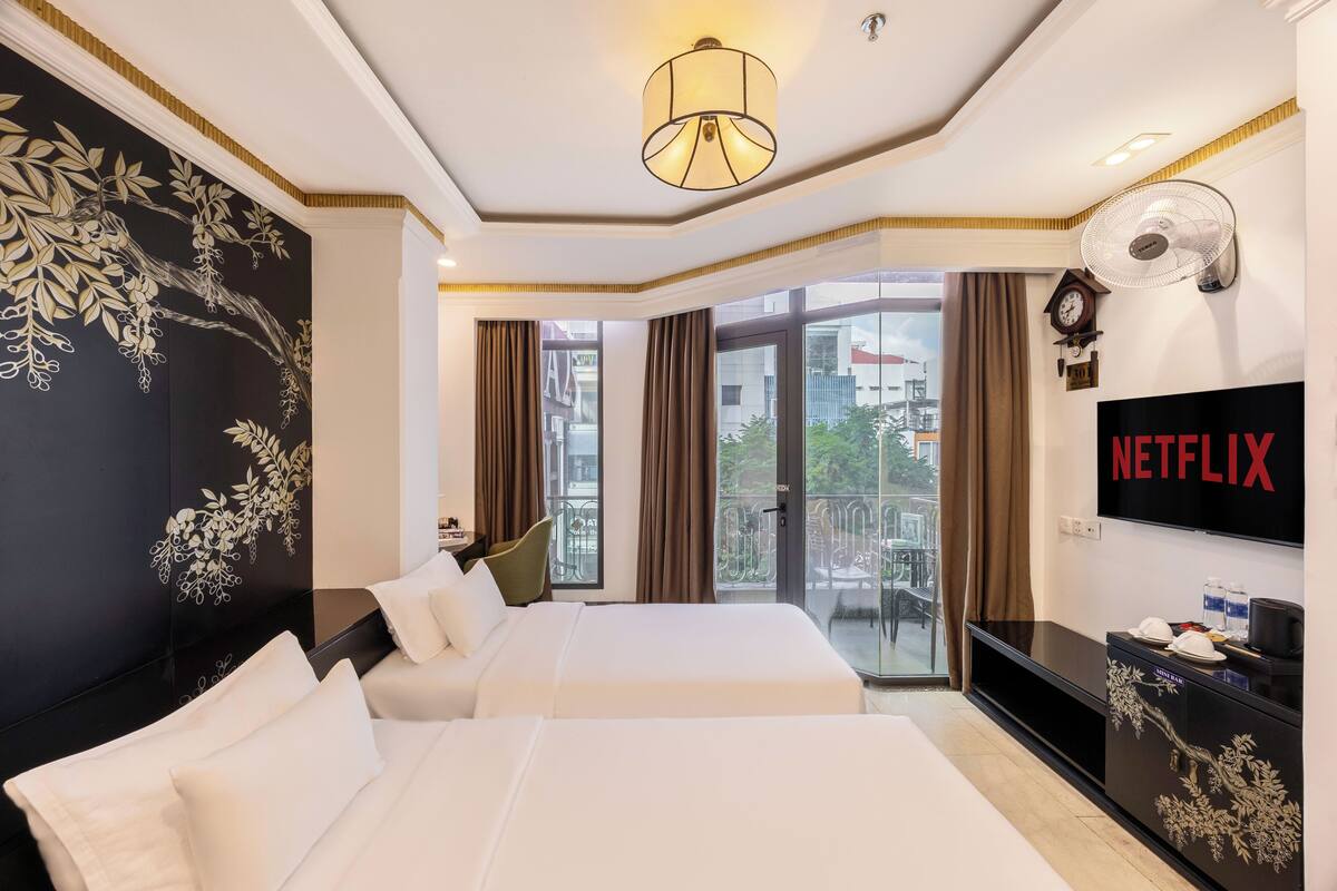 Ein Hotelzimmer mit zwei Betten, einem großen Fenster, einem Wand-Fernseher und einem Balkon mit Blick auf die Stadt.