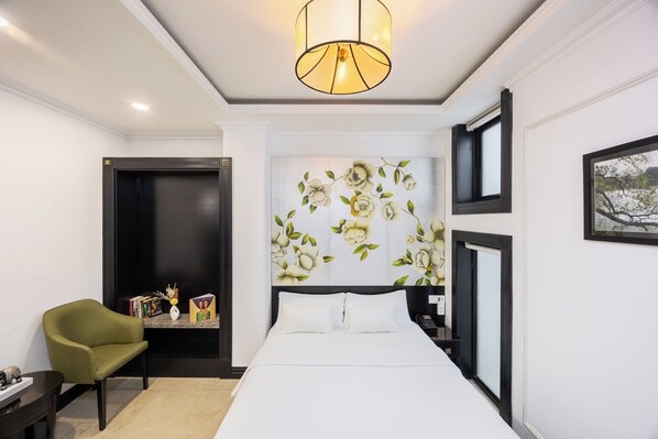 Une chambre d’hôtel avec un lit, un fauteuil vert, une table de chevet, une œuvre d’art accrochée au mur et un luminaire au plafond.