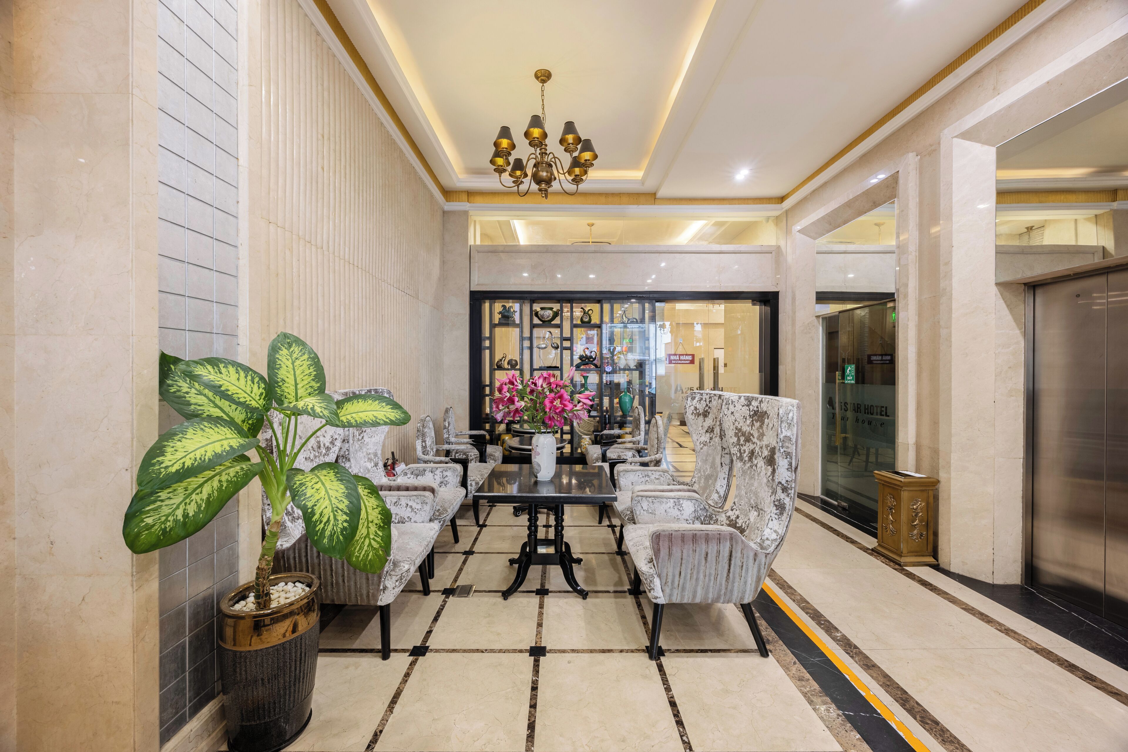 A lobby with a chandelier, seating area, and a large potted plant.