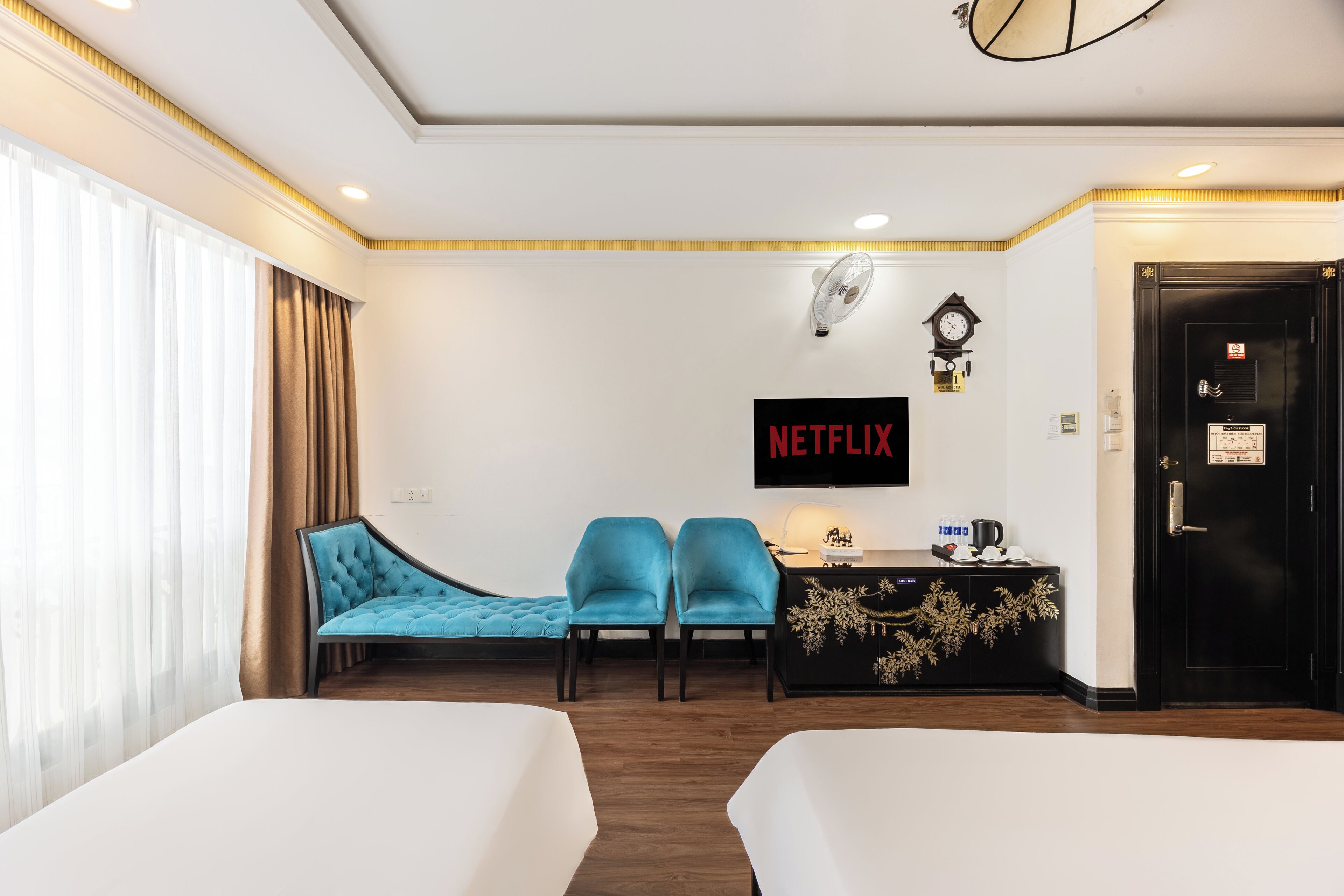 A hotel room with two beds, a desk with a coffee maker, a clock, and a wall-mounted TV displaying 'NETFLIX'.