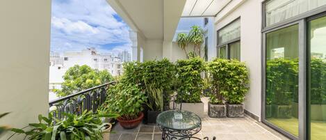 A balcony with potted plants, a glass table, and a chair.
