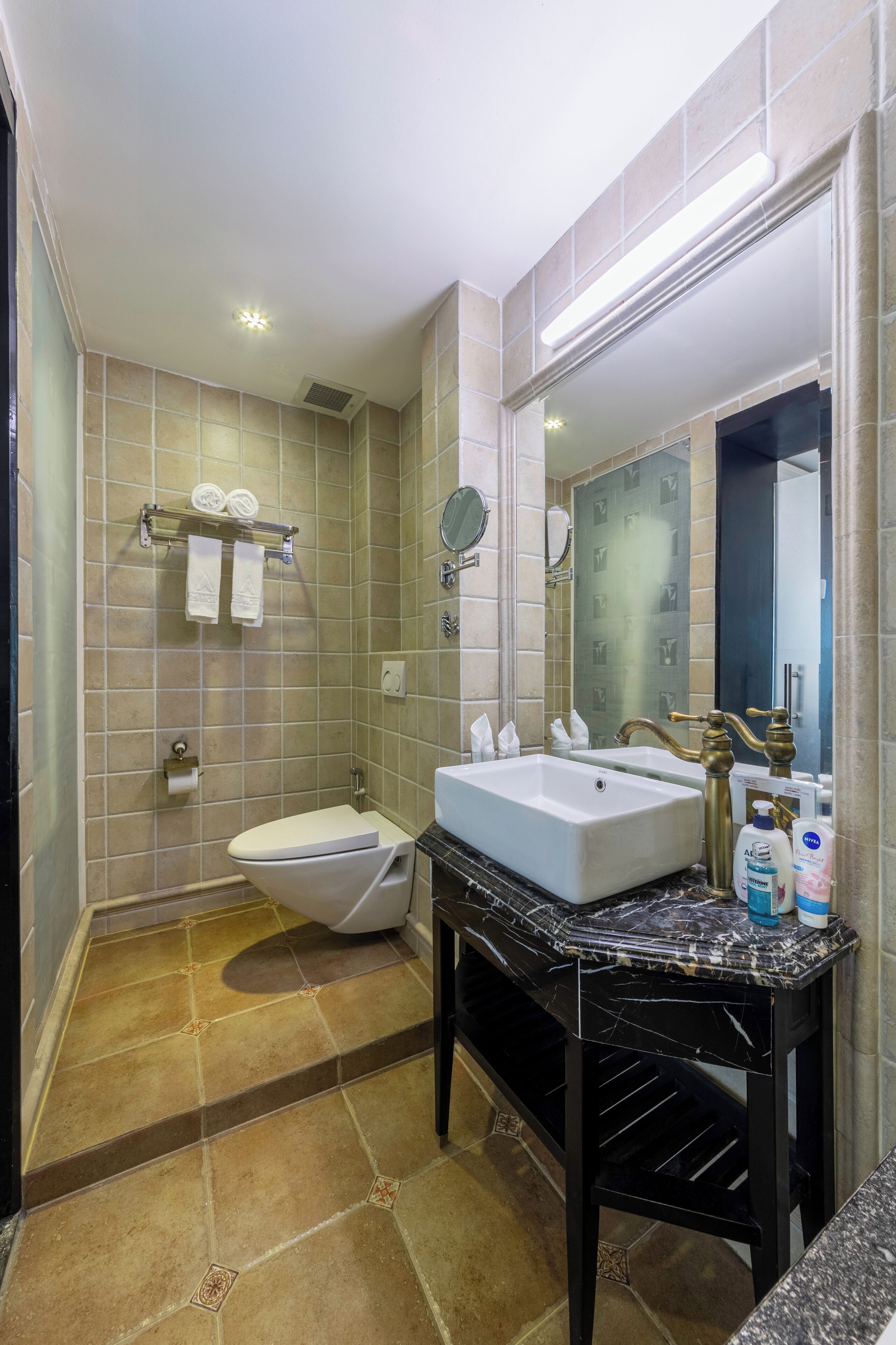 A bathroom with a white toilet, a large sink, a mirror, and a shelf with towels.
