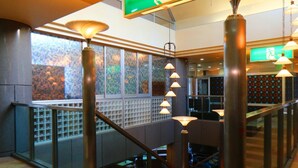 Un moderno vestíbulo de hotel con una escalera de cristal, barandillas de metal e iluminación colgante.