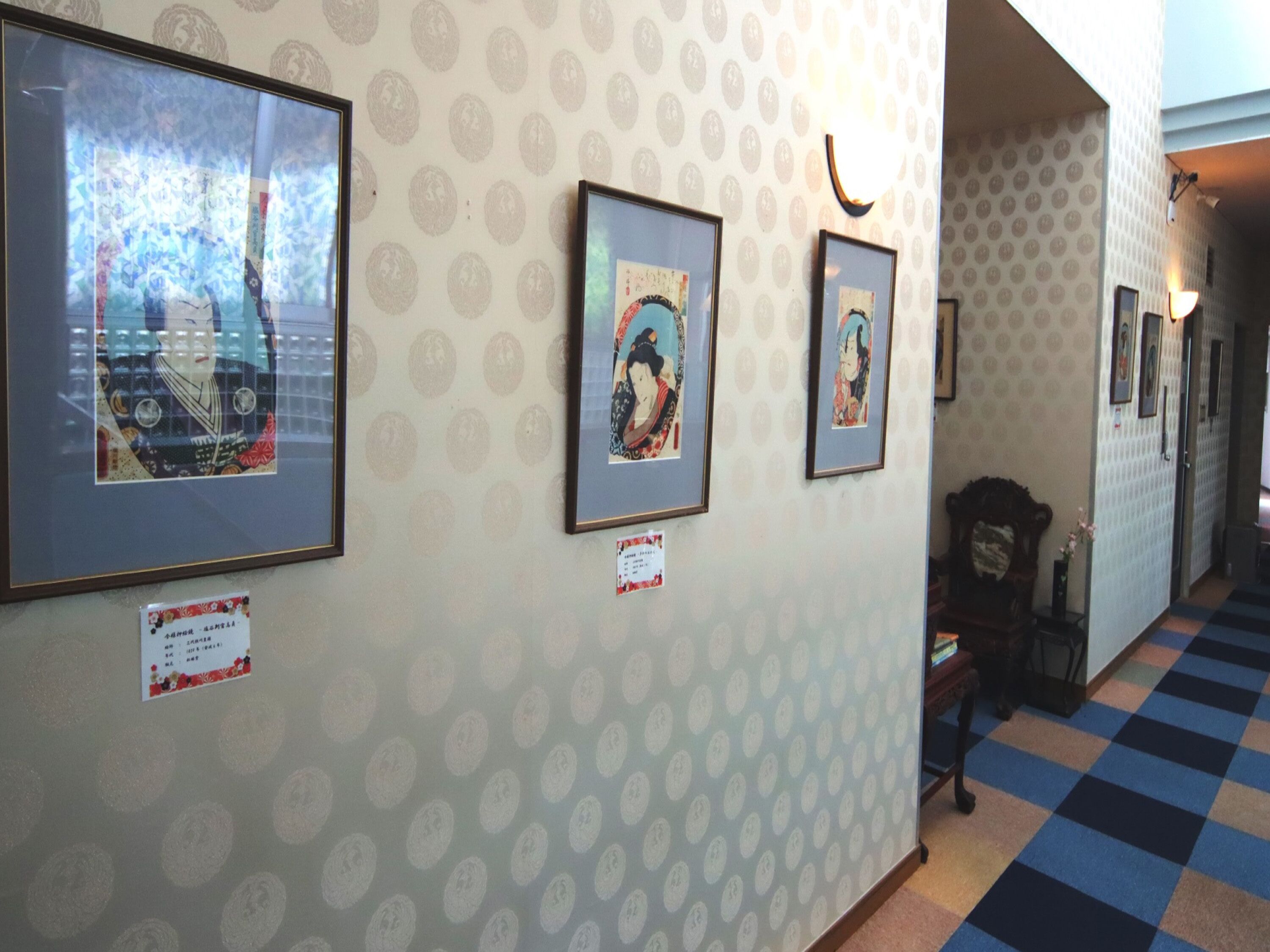 A hallway with patterned wallpaper, framed artwork on the walls, and a checkered floor.