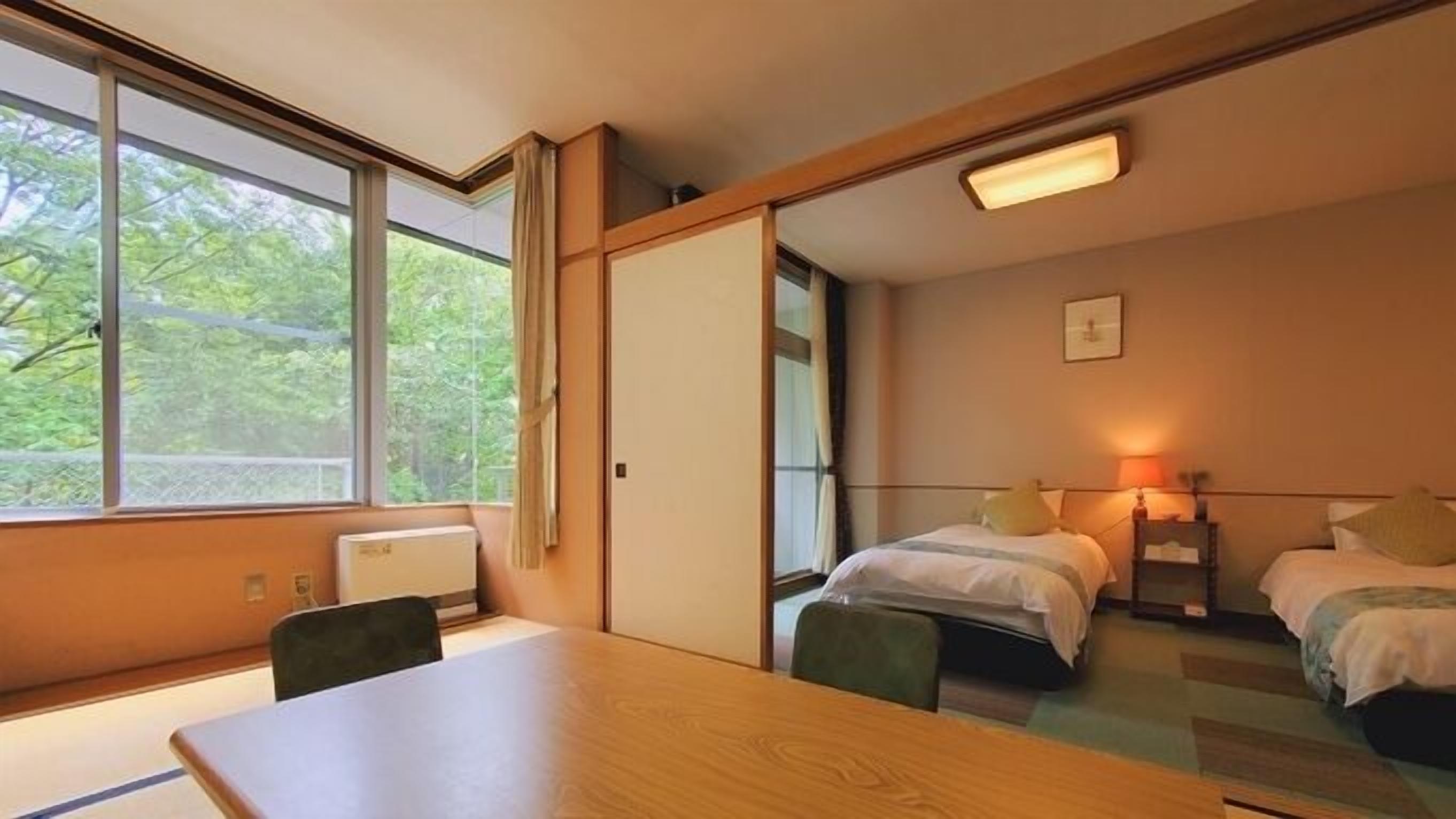 Habitación de hotel con una mesa de madera, dos camas, una ventana con vista a árboles y una lámpara en el techo.