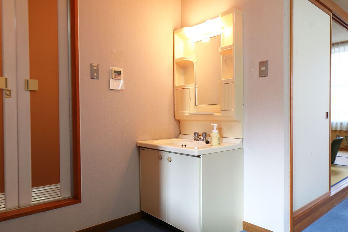 Um banheiro de hotel compacto com pia, espelho e luminária fixada na parede.