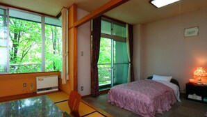 Habitación de hotel con cama, una mesa y una silla. Se ve una ventana con vistas a árboles.