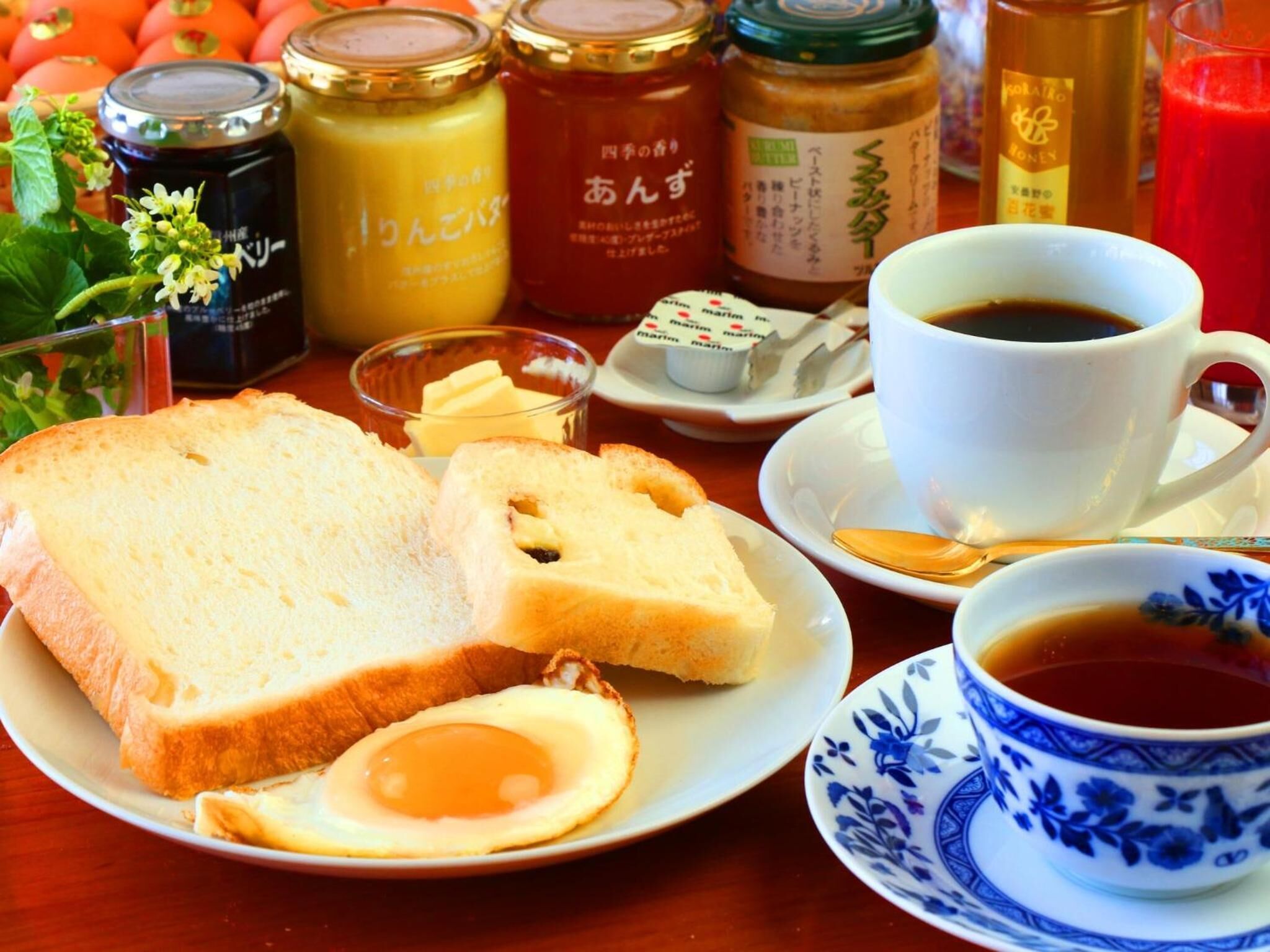 A breakfast setting with bread, an egg, butter, jam, honey, and coffee.