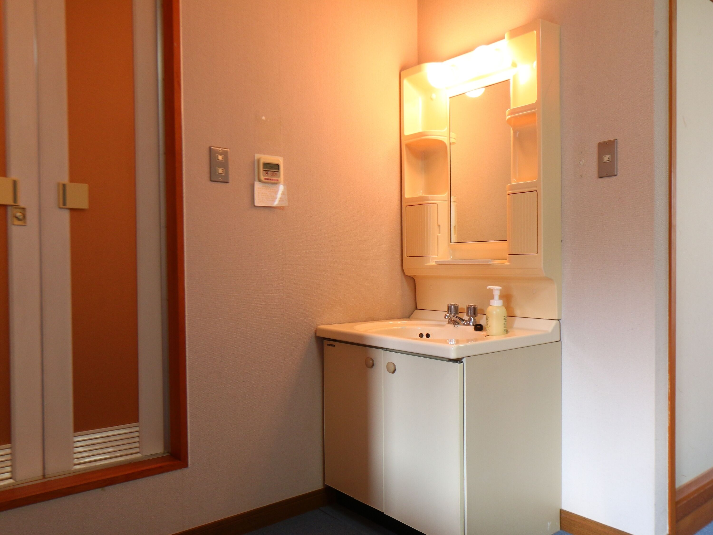 Un baño pequeño y funcional con lavamanos, espejo y una lámpara en la pared.