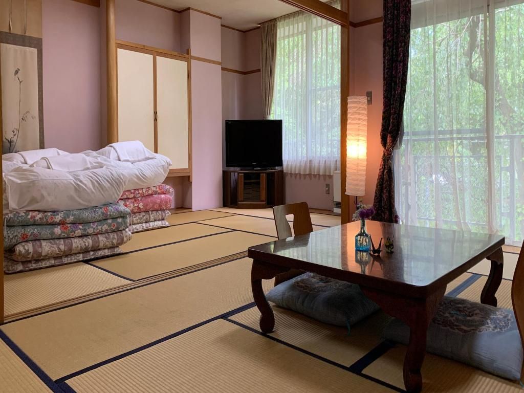 Une pièce de style japonais traditionnel, avec un sol recouvert de tatamis, une table basse, un téléviseur et un lit agrémenté d’une literie à motifs floraux.