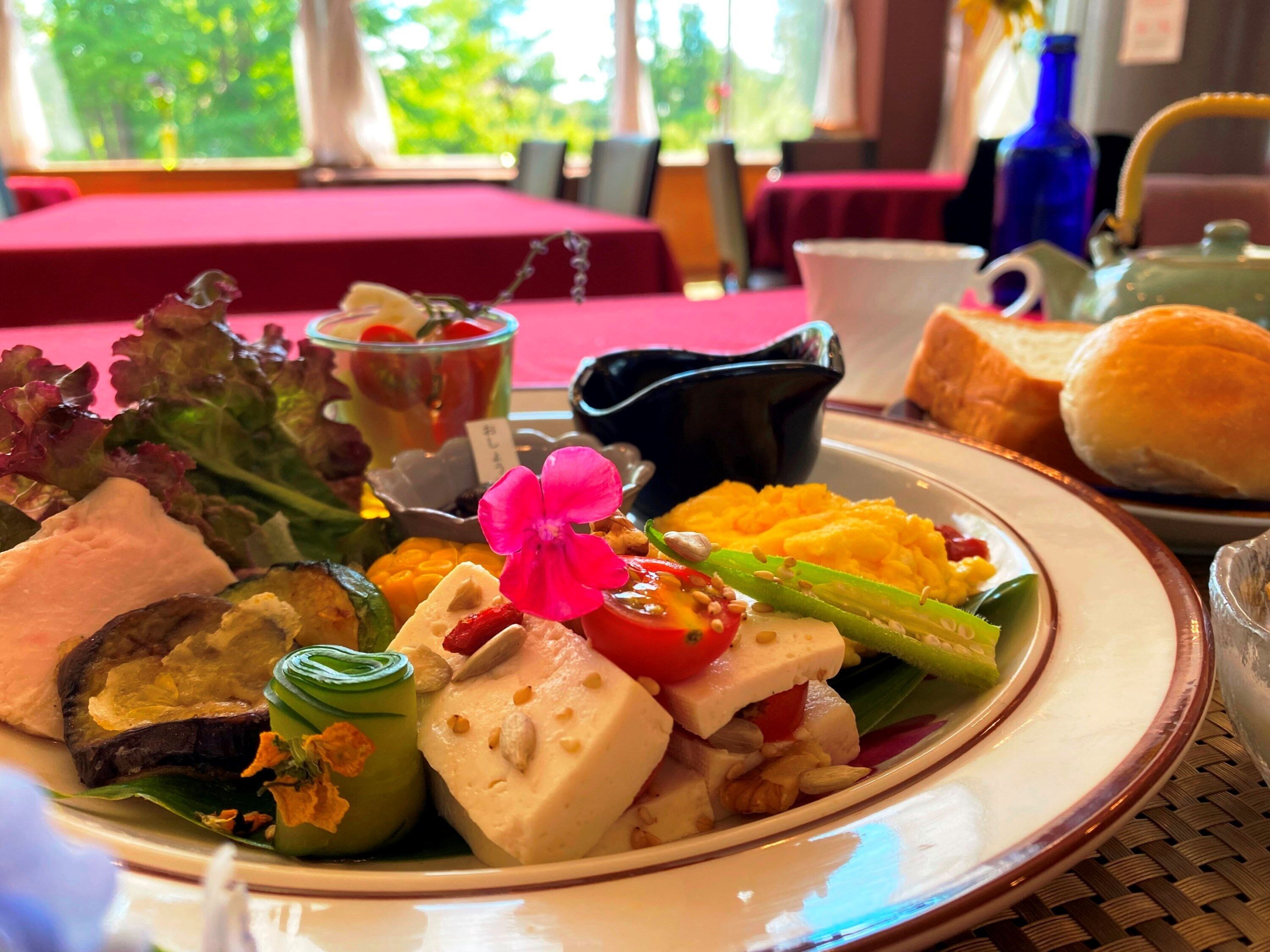A dining table with a variety of dishes, including a plate with cheese, vegetables, and a pink flower garnish.