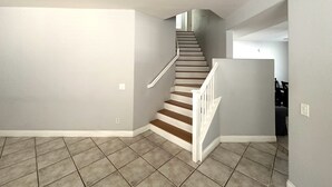 A staircase with a wooden finish and white railings, leading to a landing with a view of a room with a dark-colored sofa. - County Licensed STR! Comfortable, spacious home 15 minutes to The Strip (Las Vegas)