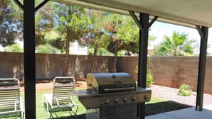 A barbecue grill under a covered patio with a brick wall and greenery in the background. - County Licensed STR! Comfortable, spacious home 15 minutes to The Strip (Las Vegas)
