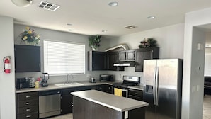 A modern kitchen with dark cabinets, stainless steel appliances, and a central island. - County Licensed STR! Comfortable, spacious home 15 minutes to The Strip (Las Vegas)