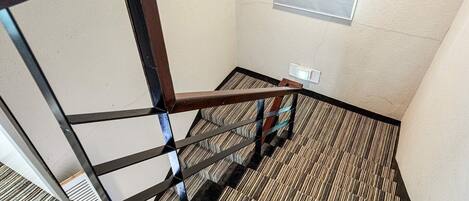 A staircase with a metal railing, carpeted floor, and a light switch on the wall.