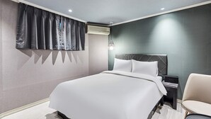 Quarto de hotel moderno com uma cama grande, uma mesa de cabeceira, uma cadeira e uma janela com cortinas.