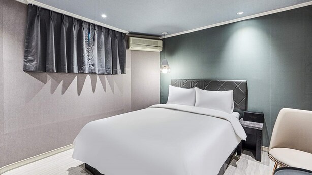 Ein modernes Hotelzimmer mit einem großen Bett, einem Nachttisch, einem Sessel und einem Fenster mit Vorhängen.