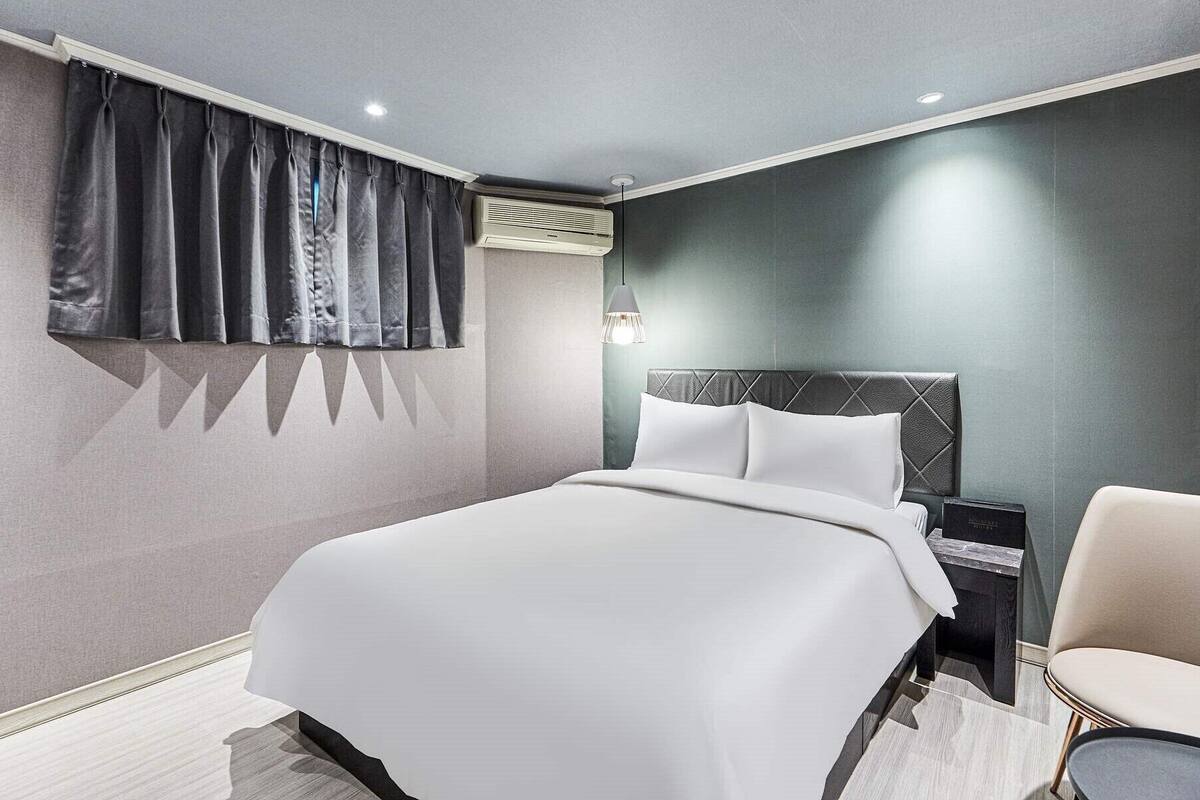 Ein modernes Hotelzimmer mit einem großen Bett, einem Nachttisch, einem Sessel und einem Fenster mit Vorhängen.