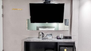 Ein modernes Hotelzimmer mit einem großen Flachbildfernseher, der über einer Marmorplatte angebracht ist, einer kleinen Küchenzeile mit einer Kaffeemaschine und einem kompakten Kühlschrank.