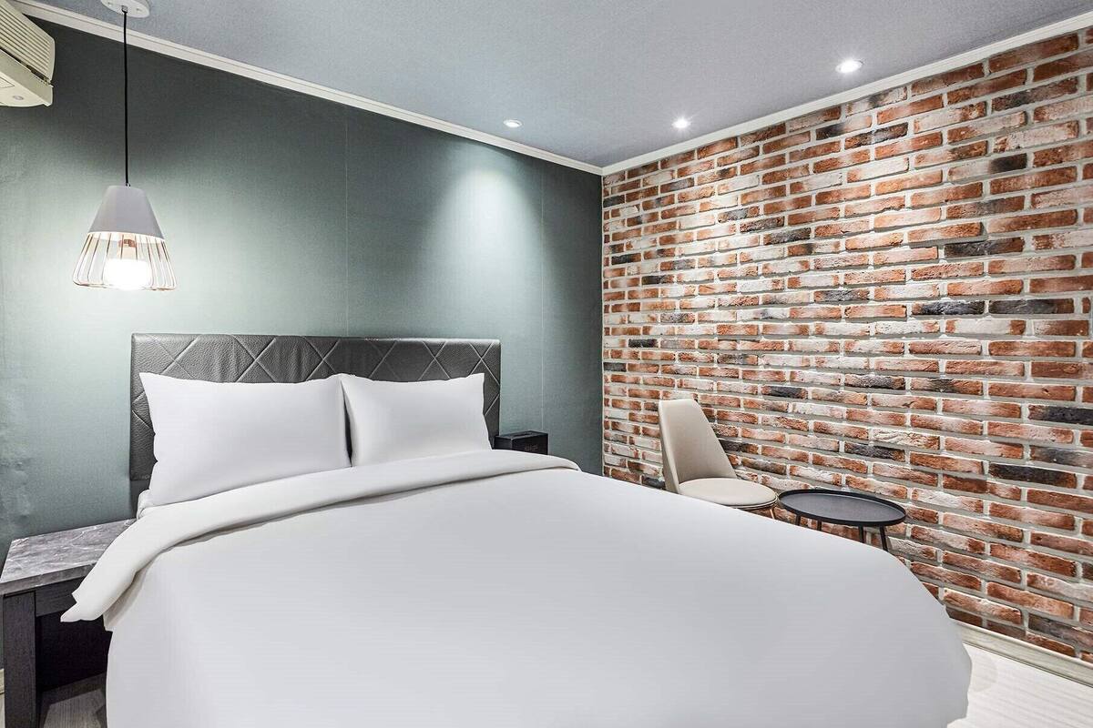 Ein modernes Schlafzimmer mit Backsteinwand, einem Bett mit weißen Leinen, einem Nachttisch, einem Sessel und einem kleinen Tisch.