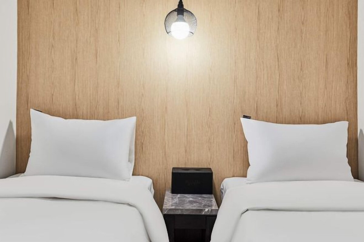 Une chambre d’hôtel avec deux lits, une tête de lit en bois, une table de chevet avec une lampe et une boîte posée sur la table de chevet.