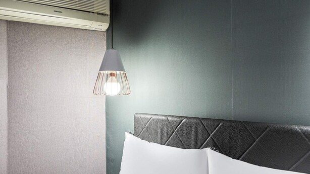 Quarto de hotel moderno com parede cinza texturizada, cabeceira estofada cinza e almofada branca.
