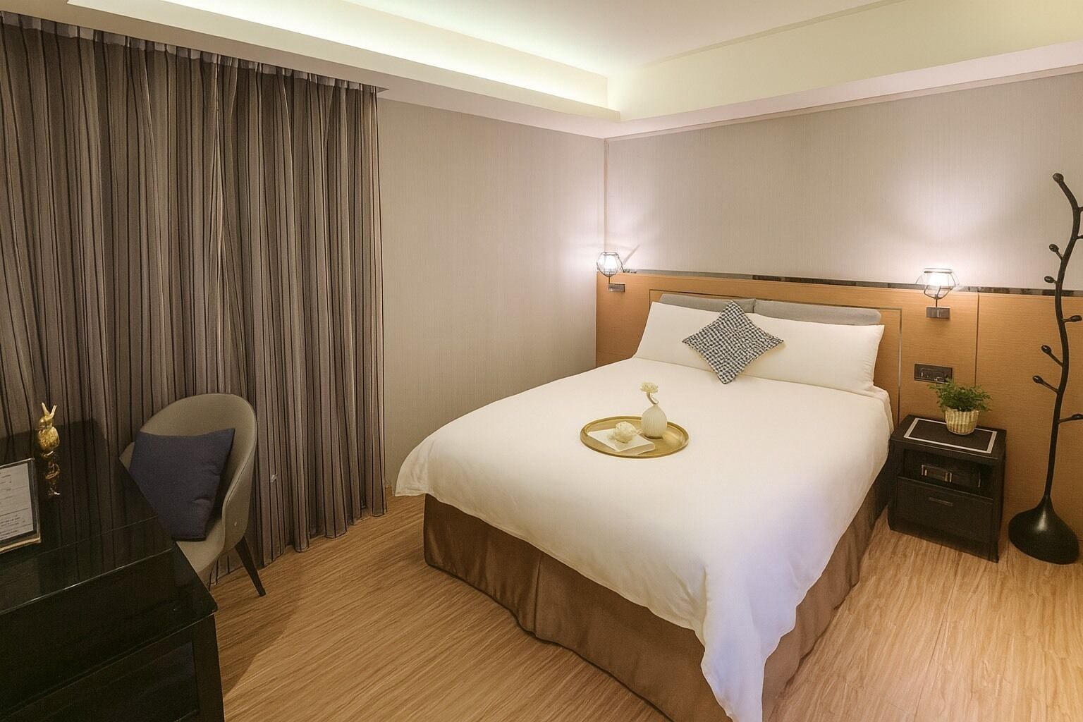A hotel room with a large bed, a chair, a desk, and a nightstand with a lamp.