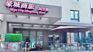 L’extérieur de l’hôtel Hope City MingSheng présente une façade moderne, une entrée abritée et un petit espace extérieur aménagé avec des parasols.