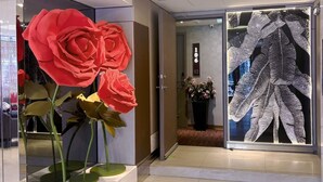 Un hall d’hôtel orné d’une grande sculpture représentant une rose rouge, d’une vitrine en verre décorée d’un motif de feuilles et du chiffre « 106 » peint sur le mur.