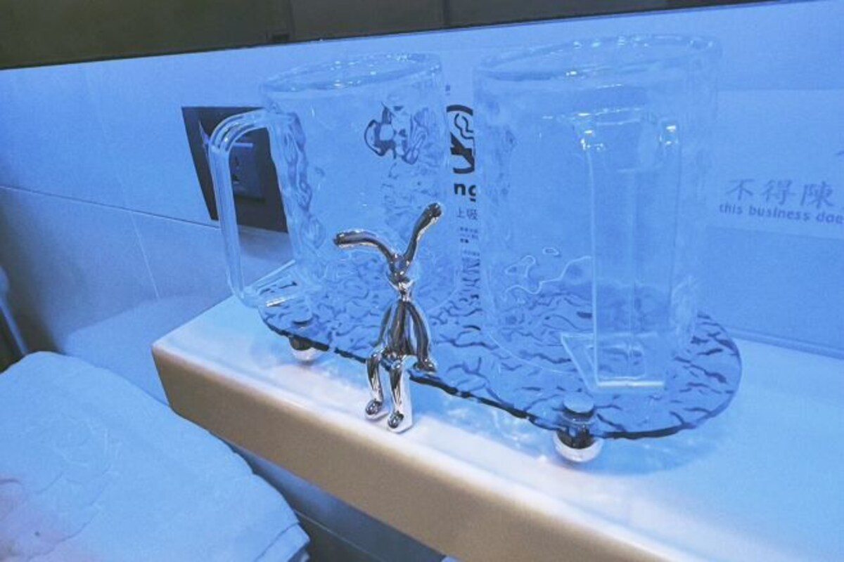 Une vitrine transparente en verre, dans laquelle se trouve une figurine en métal posée sur un socle, le tout placé sur une surface carrelée.